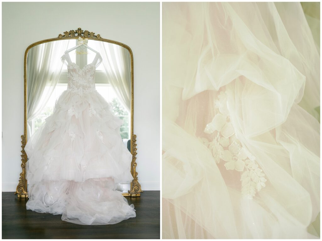 A fluffy, white, fairytale wedding dress hangs in front of a gold-framed mirror.
