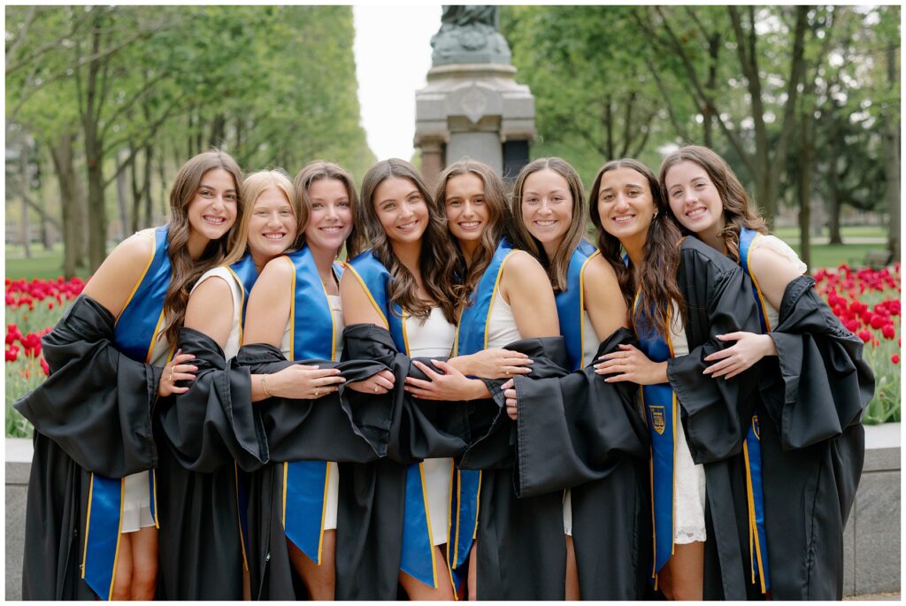University of Notre Dame graduates smiling together near the Jesus statue surrounded by blooming spring tulips.