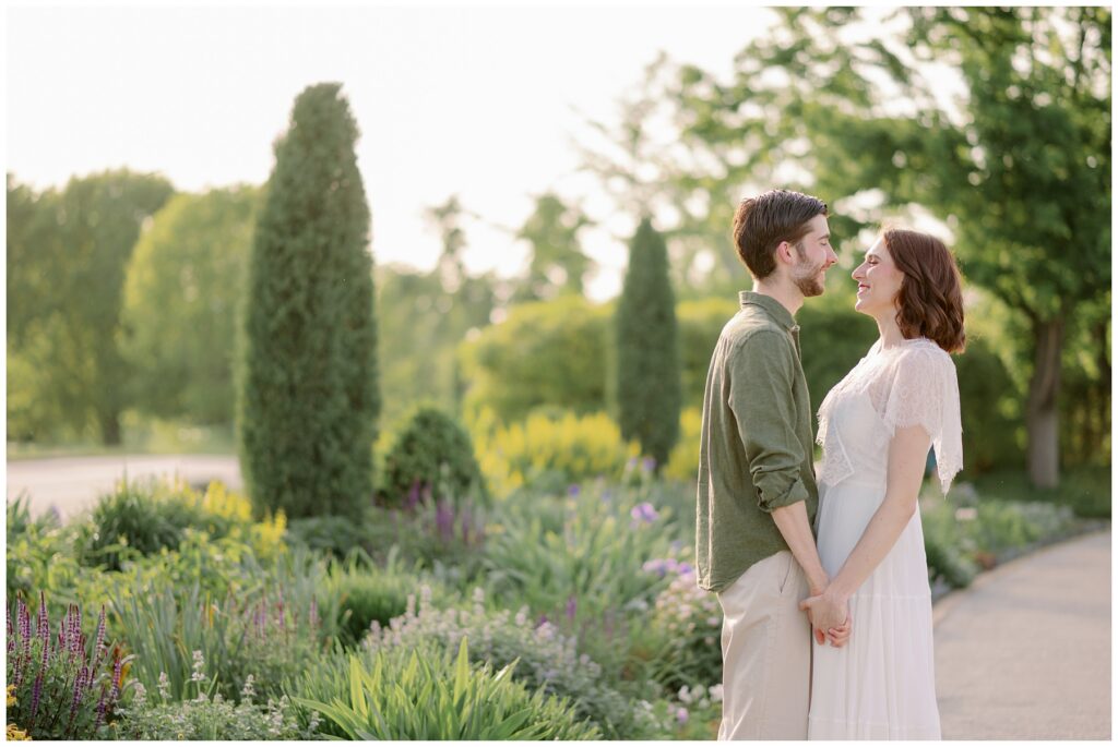 Couple holding hands and smiling at each other in a lush garden during golden hour in Forest Park