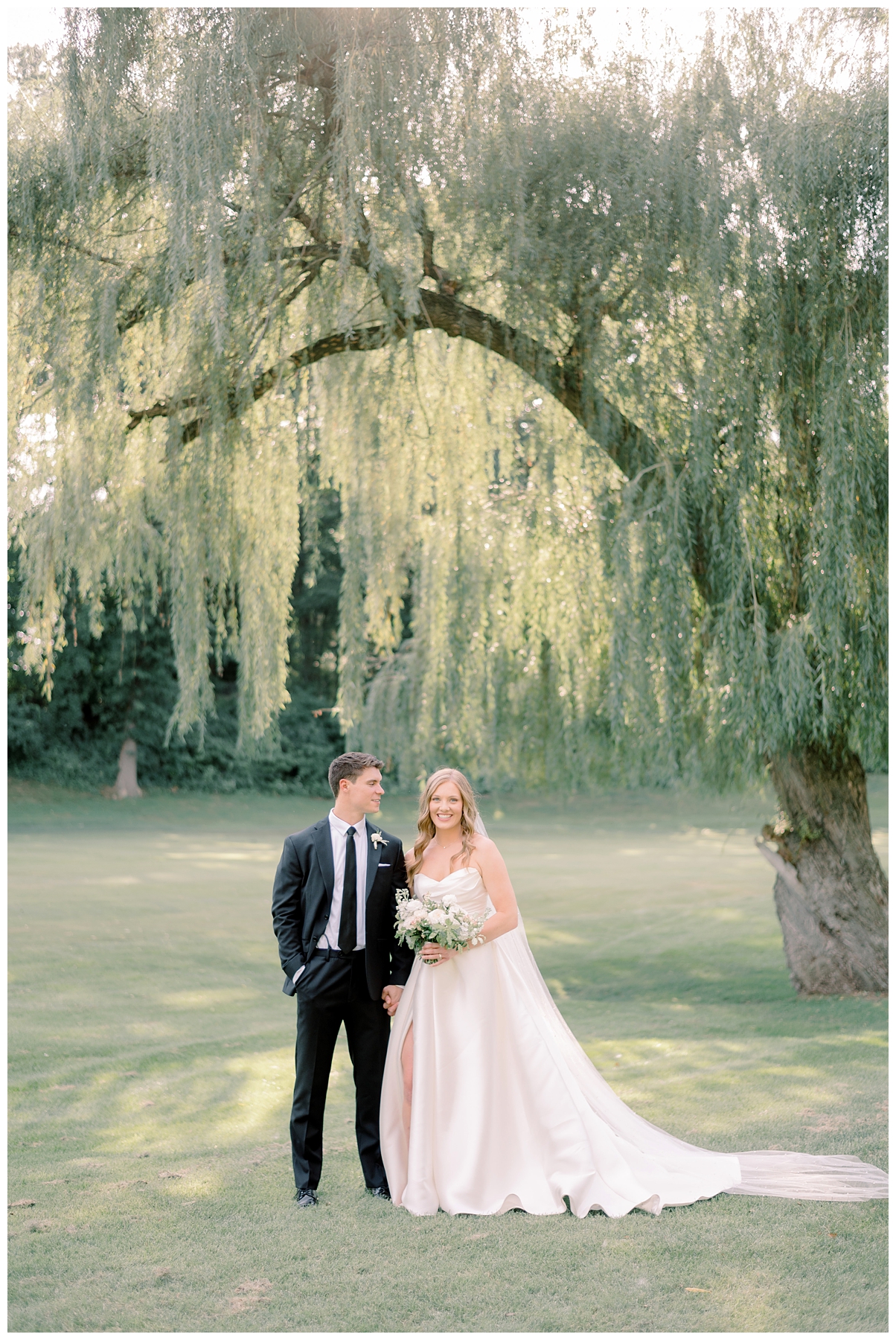A newlywed couple stands under a willow tree in one of the best places to take wedding photos in South Bend