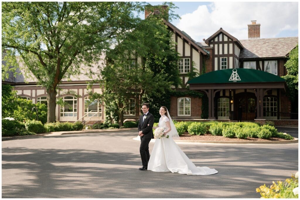 Bride and groom walk hand in hand outside Hinsdale Golf Club in Clarendon Hills, Illinois, during their timeless black tie wedding on a sunny June afternoon.