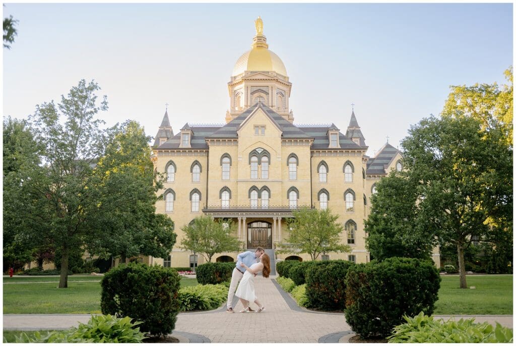 Couple sharing a kiss in front of the Golden Dome during summer University of Notre Dame engagement photos.